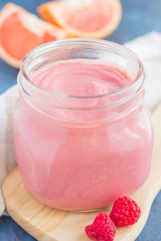 two raspberries sit on a cutting board next to a jar of yogurt