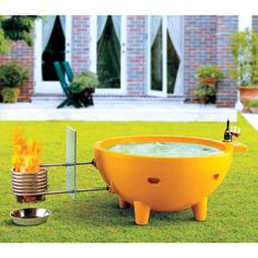 a large yellow bathtub sitting on top of a lush green field next to a fire pit