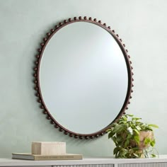 a round mirror sitting on top of a wooden shelf next to a potted plant