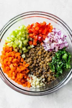 chopped vegetables in a glass bowl on a white counter top, including carrots, celery, onions and lentils