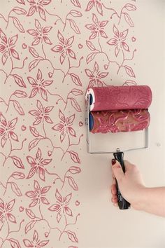 a person using a paint roller to paint a wall with pink and white flowers on it