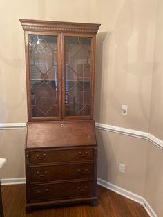 a wooden cabinet sitting on top of a hard wood floor next to a white wall