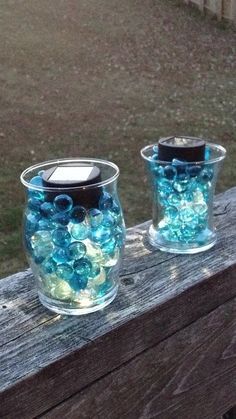 two glass vases filled with blue and green beads sitting on a wooden fence post