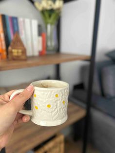 a person holding a coffee cup in front of a book shelf with books on it