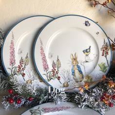 three white plates with blue rims decorated with flowers and rabbits, surrounded by silver tinsel