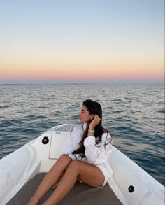 a woman sitting in the back of a boat on top of the ocean at sunset