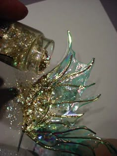 a hand is holding a small glass object with glitter on it's wings and leaves