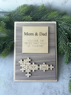 a wooden puzzle with the words mom and dad on it next to some pine branches