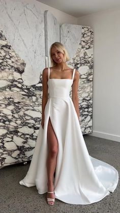 a woman standing in front of a marble wall wearing a white dress with thigh high slit