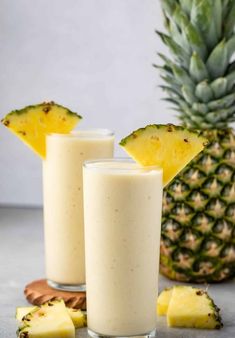 two glasses filled with pineapple smoothie on top of a table next to sliced pineapples