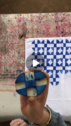 a woman holding up a piece of art with blue and white designs on the wall behind her