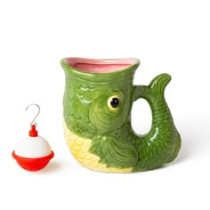 a green ceramic fish mug next to a red ornament on a white background