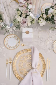 the table is set with gold and white plates, napkins, silverware, and flowers