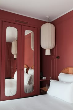 a bedroom with red walls and white bedding, two large mirrors on the wall