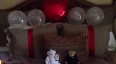 two figurines sitting on top of a bed next to a red heart shaped balloon