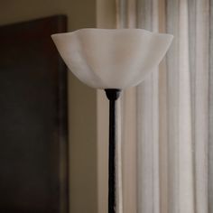 a lamp that is next to a window with curtains in the background and a curtained wall behind it