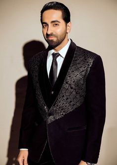 A adorned black tuxedo featuring a black velvet placket and intricate embroidery embellished with metallic beads across the chest area. Black Velvet Suit For Semi-formal Occasions, Designer Black Embellished Blazer, Designer Embellished Black Blazer, Luxury Black Embellished Blazer, Traditional Black Formal Blazer, Luxury Velvet Suit For Black-tie Events, Tailored Black Embroidered Suits, Luxury Velvet Suits For Parties, Velvet Tuxedo For Winter Party