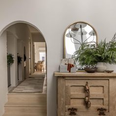 an entry way with a mirror, potted plant and wooden dresser