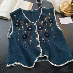 a blue sweater with flowers on it sitting on a table next to an open book