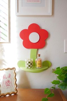 a red flower on a green shelf next to a potted plant and framed pictures