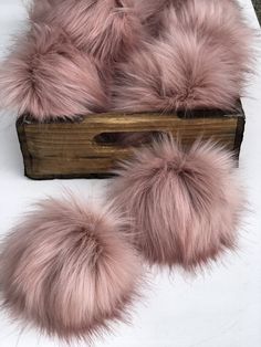 three pink fur pom - poms on top of a wooden box with white sheets