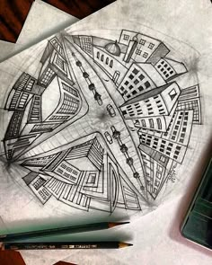 a pencil drawing of a cityscape with buildings and roads on paper next to a cell phone