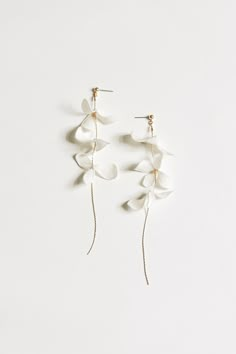 two white flowers hanging from the side of a pair of gold earwires on a white background