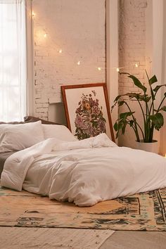 an unmade bed with white sheets and pillows in front of a brick wall decorated with lights