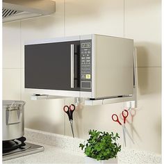 a microwave mounted to the side of a wall above a potted plant and scissors