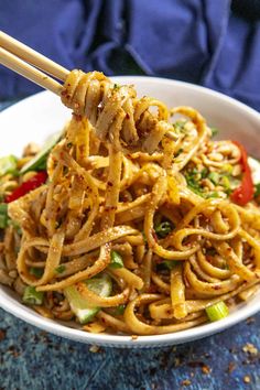 a white bowl filled with noodles and veggies on top of a blue table