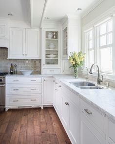 a kitchen with white cabinets and wood floors is pictured in this image, there are flowers on the counter