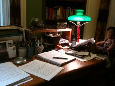 a woman sitting at a desk in front of a lamp and papers on the table