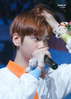 a young man holding a microphone up to his face while wearing an orange and white shirt