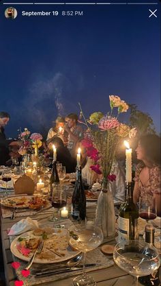 a group of people sitting around a table with food and drinks on it at night