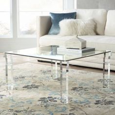 a glass coffee table sitting on top of a rug in front of a couch and window