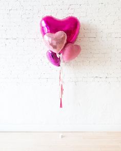 three heart shaped balloons attached to a white brick wall