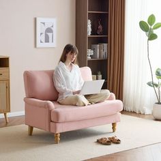 a woman sitting on a pink chair using a laptop