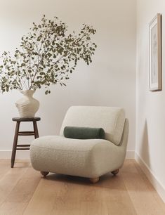 a white chair sitting in front of a vase filled with flowers on top of a hard wood floor