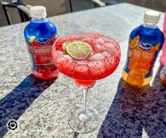 a red margarita sitting on top of a table next to bottles of soda and water