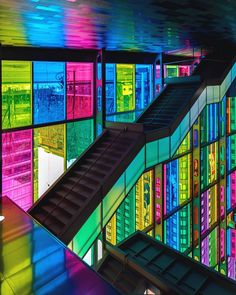 an escalator in front of multicolored glass windows with stairs leading up to them