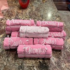 pink towels with white writing on them sitting on a granite counter top next to a red vase