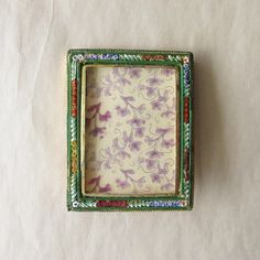 a small green and purple frame sitting on top of a white table next to a wall