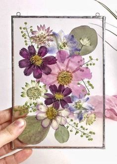 a person holding up a card with flowers on it and watercolors in the background