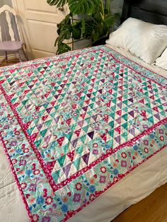 a bed with a quilt on top of it next to a chair and potted plant