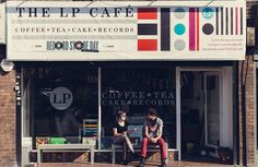 two people sitting on a bench in front of a coffee shop with the lp cafe sign above them