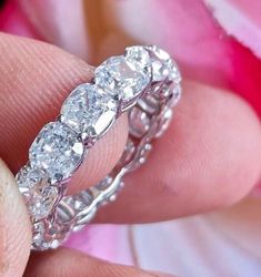 a woman's hand holding a diamond ring in front of her face with pink flowers behind it