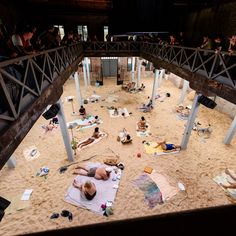 people are laying on the sand in an open area with metal structures and stairs above them