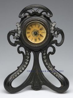 an ornate black clock with gold dial and crystal accents on the face is shown in front of a gray background