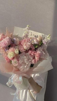 a woman holding a bouquet of pink and white flowers in her left hand, with a sign on the wall behind her