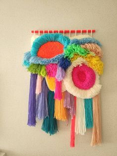 a wall hanging made out of yarn and tassels on a white wall next to a shelf